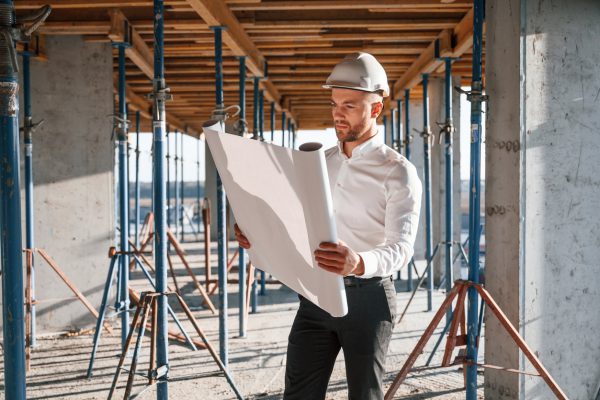 In shirt and black pants. Reading the plan. Man is working on the construction site at daytime.